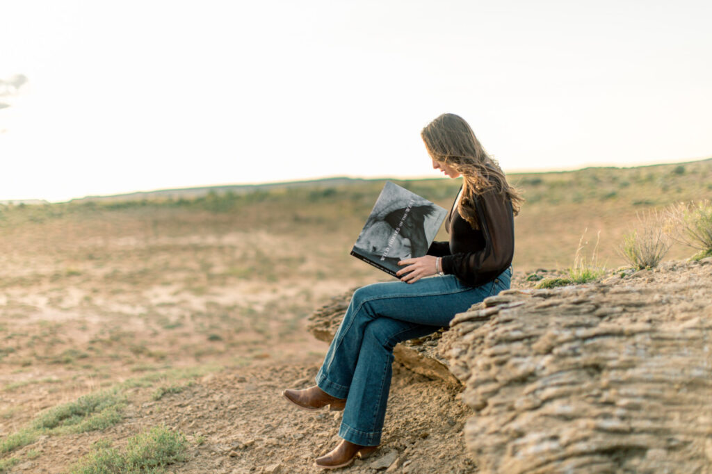 Amy McGann reading a photography book outdoors in Montana, reflecting on archetypes in branding and creative storytelling.
